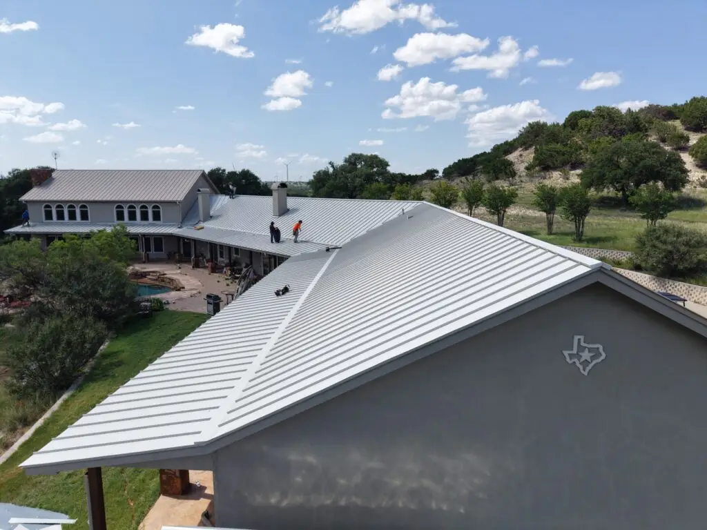 Sandstone-colored snap lock metal roof panels being installed in Texas